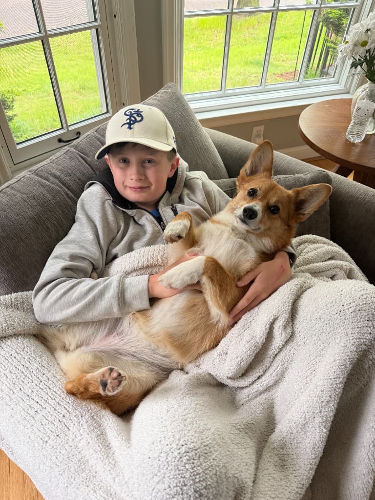 Oscar smiling with a corgi in a cozy chair at home